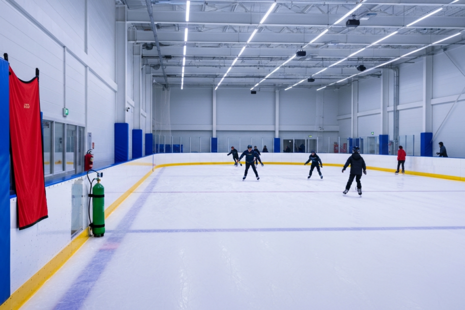 A detailed, photorealistic image of a modern, well-maintained indoor sports facility with a smooth skating rink surface, bright lighting, safety padding on walls, and emergency equipment visible in th