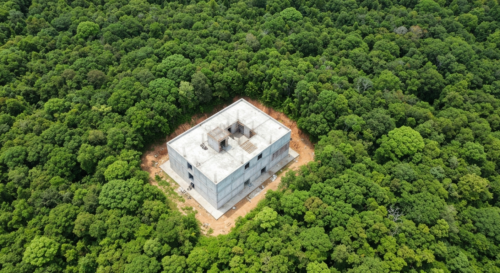 Aerial view of an illegal construction in a protected natural area, with a stark contrast between the building and the surrounding green landscape, photorealistic, high detail, environmental impact th