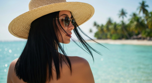 A photorealistic image of a woman with healthy, shiny hair standing on a tropical beach, wearing a wide-brimmed hat and sunglasses, with a gentle breeze blowing her hair. The background shows turquois