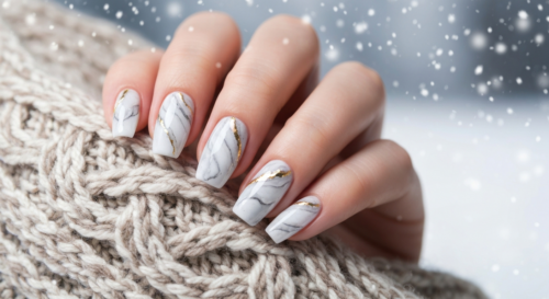 Photorealistic close-up of elegantly manicured nails with a marble effect in white and gray tones, with subtle gold accents, set against a soft winter background with snowflakes and a cozy scarf.