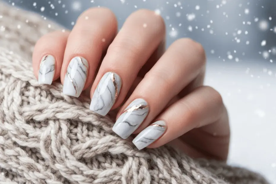 Tendencias en uñas para el invierno 2024: diseños y cuidados 17 Photorealistic close-up of elegantly manicured nails with a marble effect in white and gray tones, with subtle gold accents, set against a soft winter background with snowflakes and a cozy scarf.