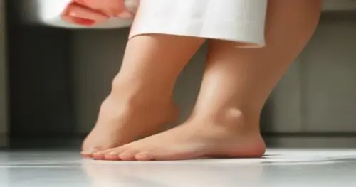 Close-up of a woman's feet with a small blister on the heel, hands applying a swipe of cocoa butter from a tin, bathroom setting, soft natural light, realistic texture, no text.