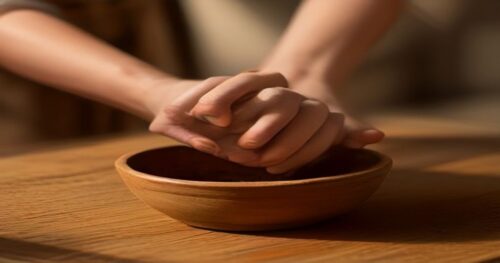Close-up of mature female hands with age spots, holding a small bowl of dark cocoa powder and a block of pure cocoa butter on a rustic wooden table, natural light, soft shadows, cosmetic skincare sett